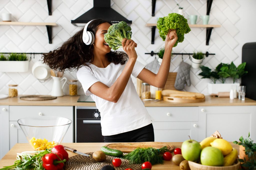A lady dancing with salad leaves and broccoli on the modern kitchen 